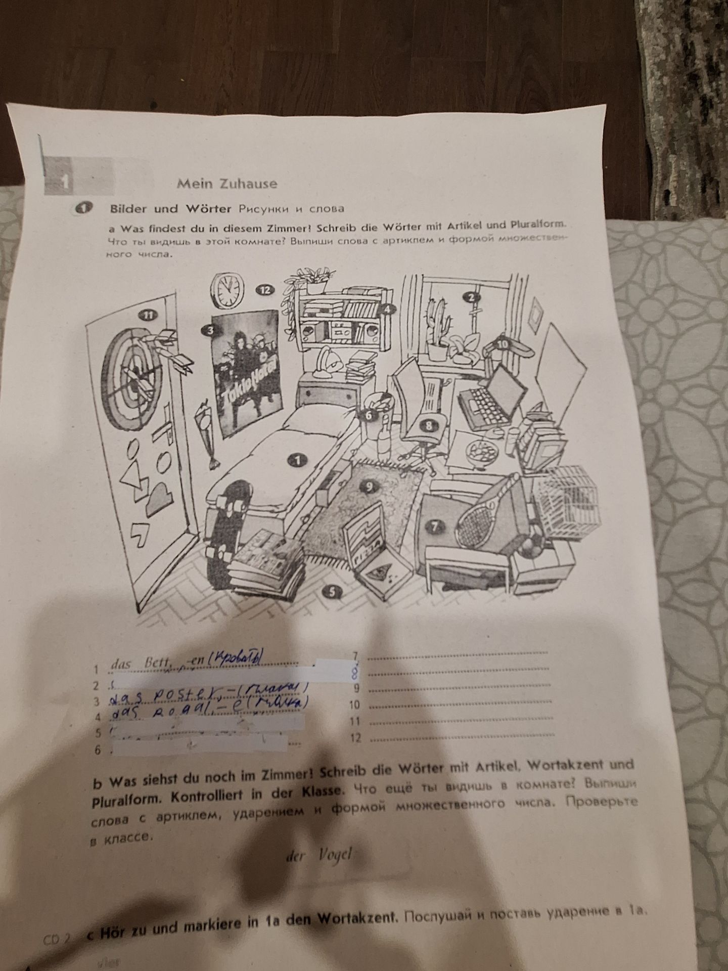 Фото задания: 1b. Was siehst du noch im Zimmer? Schreib die Wörter mit Artikel, Wortakzent und Pluralform. Kontrolliert in der Klasse.…