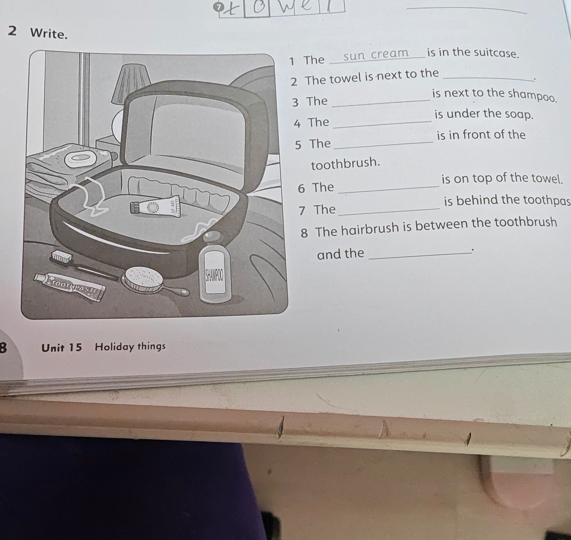Фото задания: Write. Complete the sentences using the objects in the picture: 1) The ______ is in the suitcase. 2) The towel is next to the…